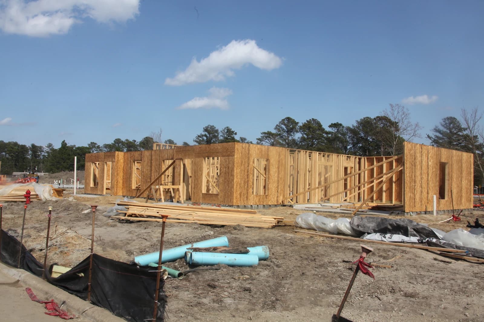 New home construction with wood framing on a dirt lot, under a blue sky.