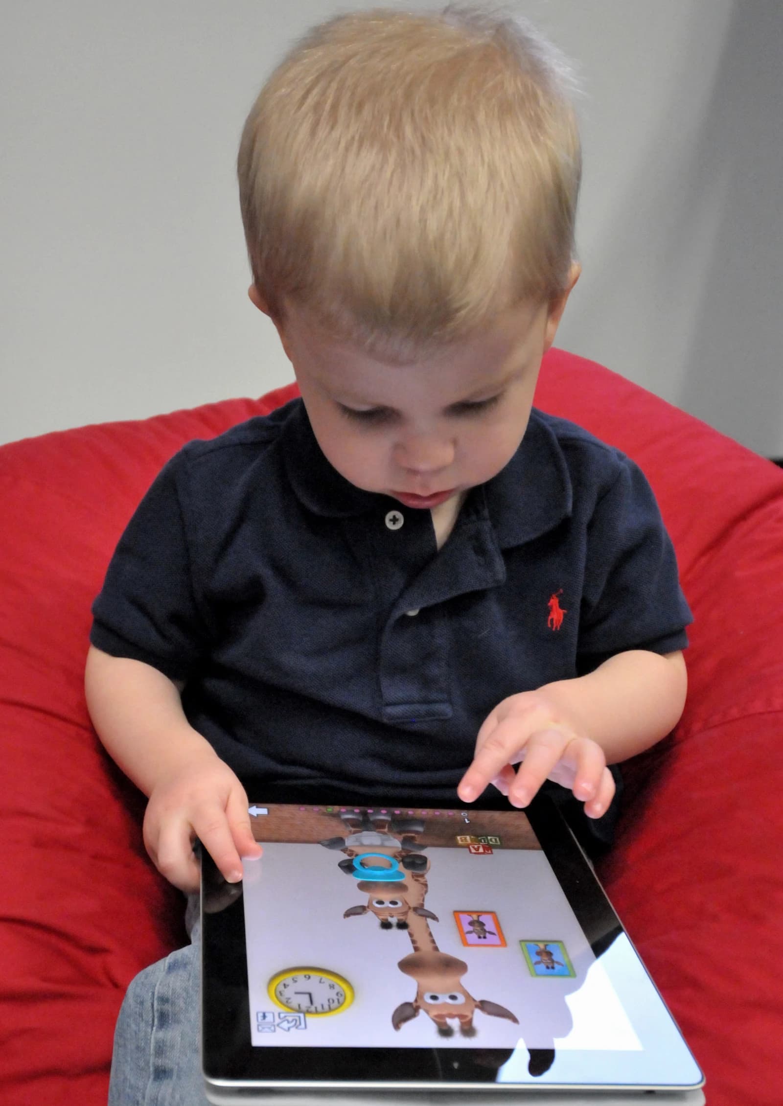 Young child playing on an iPad with a cartoon giraffe game displayed on screen.