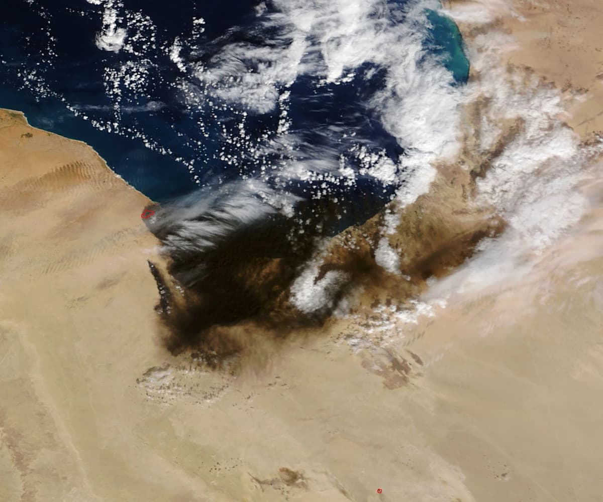 Satellite image showing a large dark smoke plume originating from the Libyan coastline.