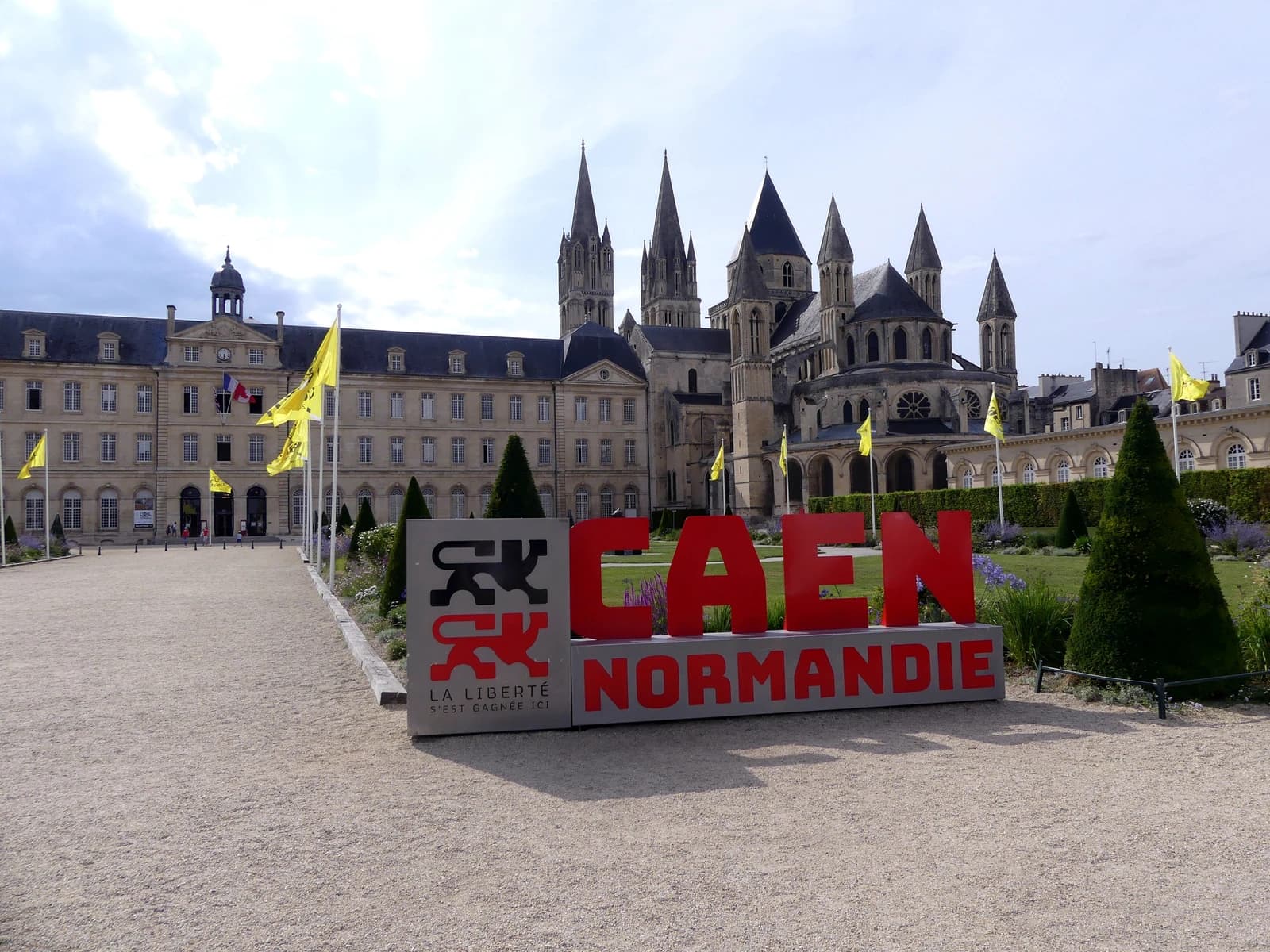 Hôtel de ville and Eglise St-Étienne de Caen with 'Caen Normandie' sign in foreground.