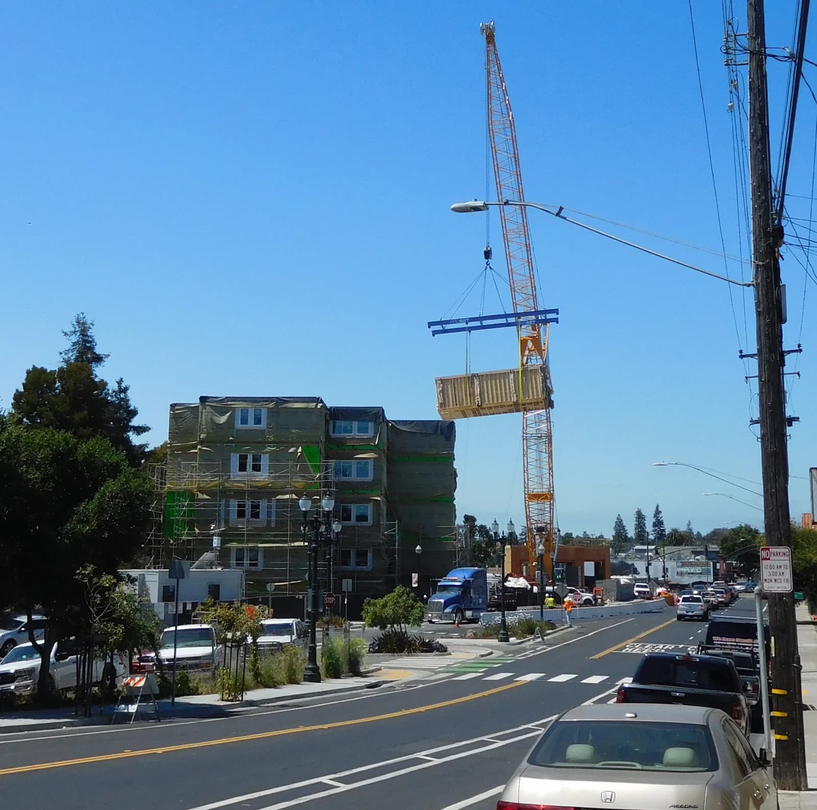 Modular housing construction site in Oakland, California, with a crane lifting a building section.