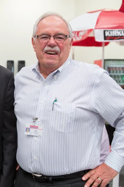 James Sinegal, co-founder of Costco, stands smiling in a pinstriped shirt.