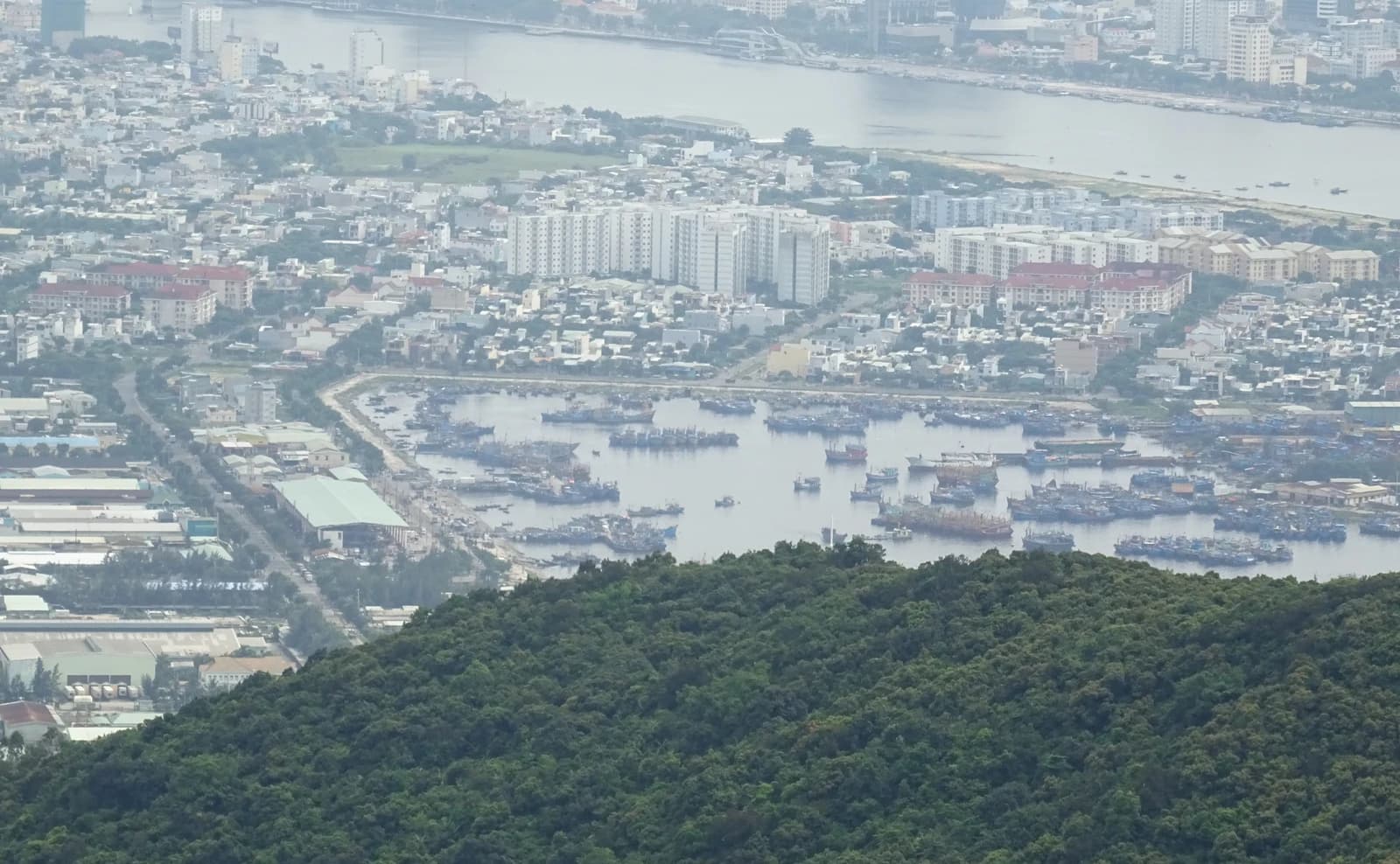 Aerial view shows Da Nang city with buildings along a river and numerous boats in a port.