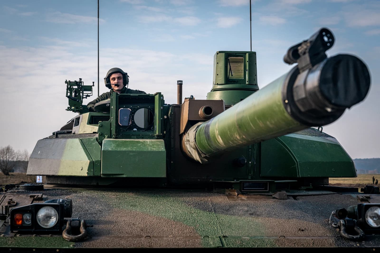 Polish soldier wearing a helmet and headset in the turret of a military tank.