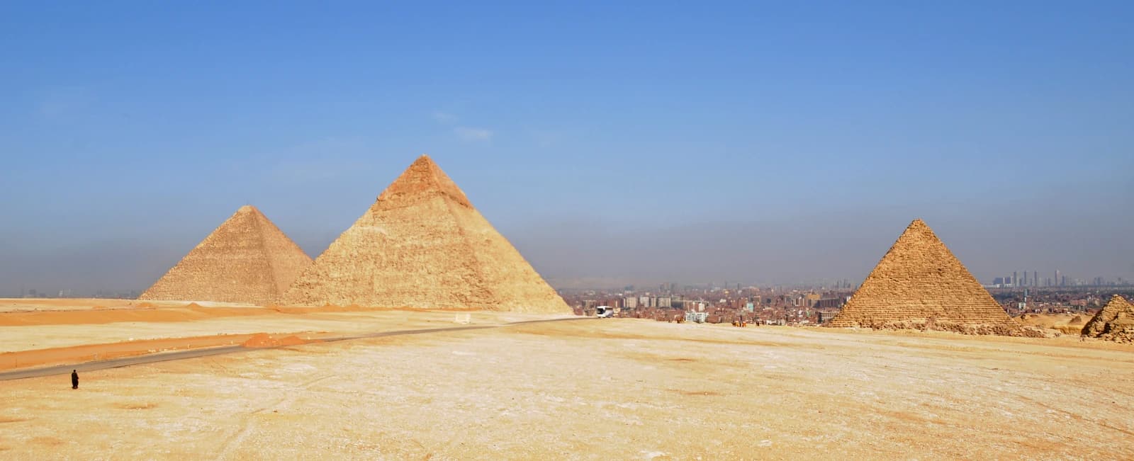 Pyramids of Giza with modern buildings of Cairo in the distant background.