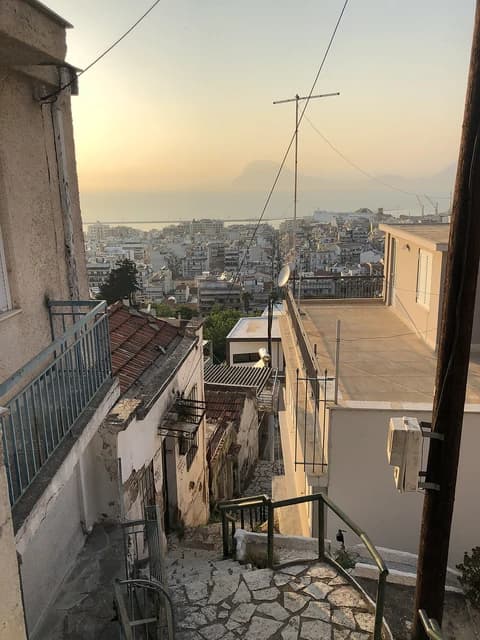 City of Patras, Greece, with residential buildings and the sea under a sunset sky.