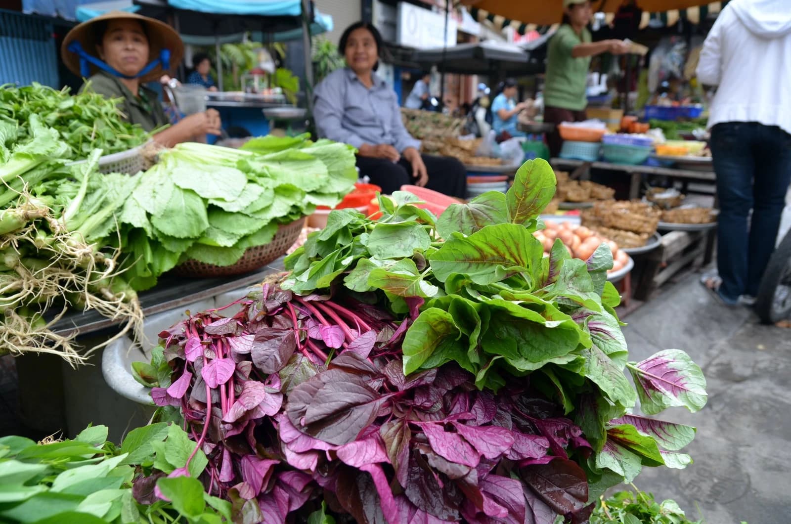 Bundles of various green and red leafy vegetables on display at a market stall.