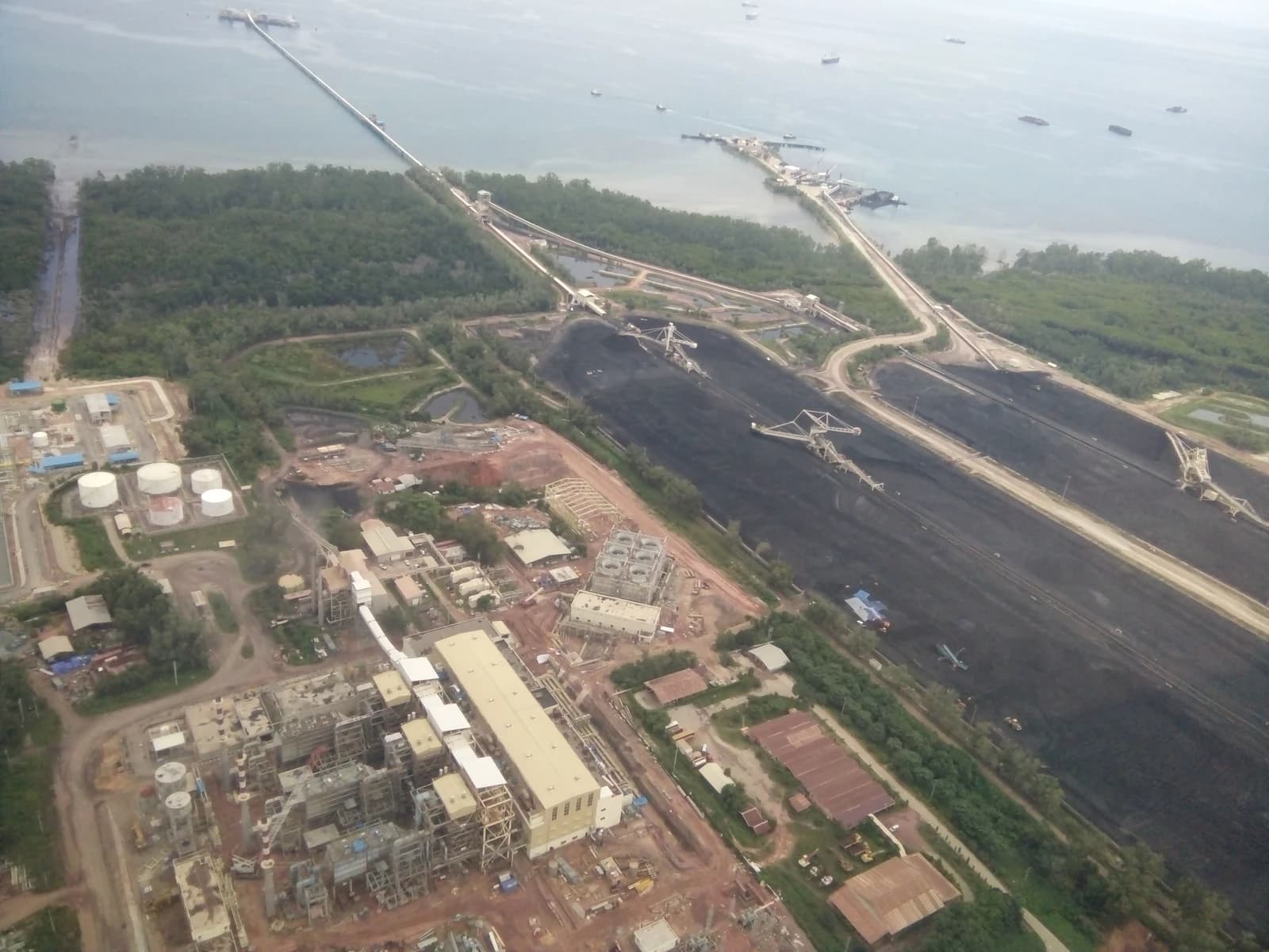 Aerial view of a coal terminal with large stockpiles, industrial buildings, and a long pier extending into the water.