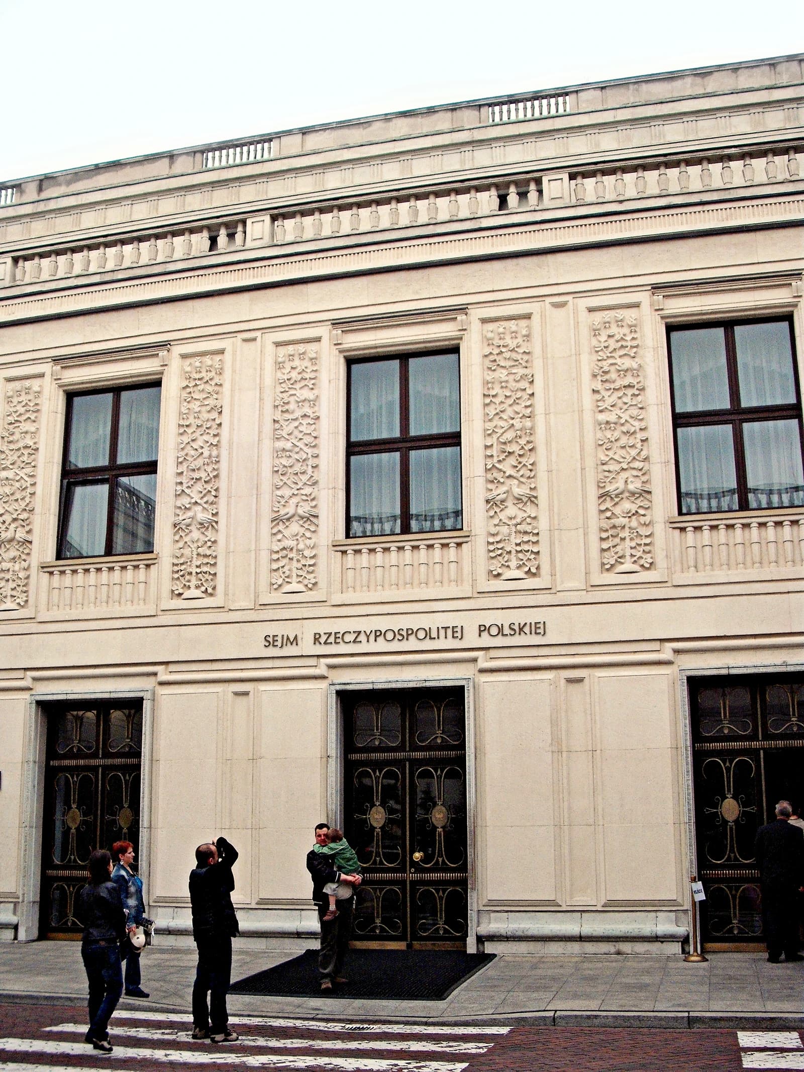 Exterior of the Polish Parliament (Sejm) building with text "SEJM RZECZYPOSPOLITEJ POLSKIEJ" above doors.