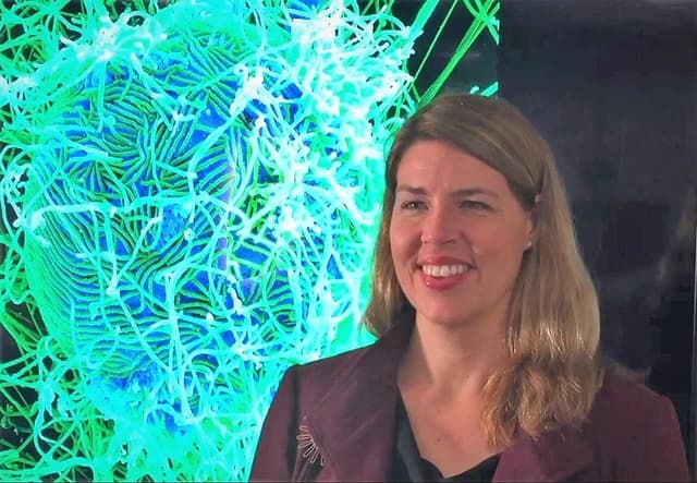 Erica Ollmann Saphire, a scientist, is shown next to a microscopic image of a virus-infected cell.