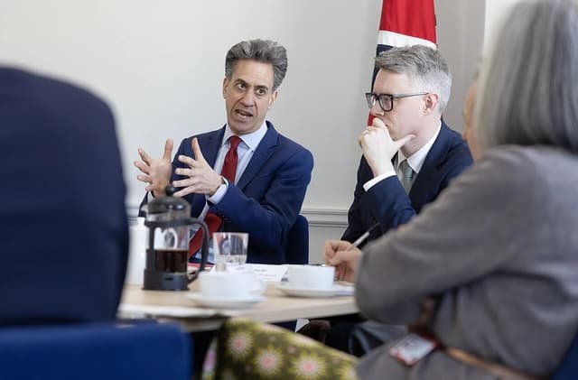 Ed Miliband, Secretary of State, speaking with hands gesturing at a conference table.