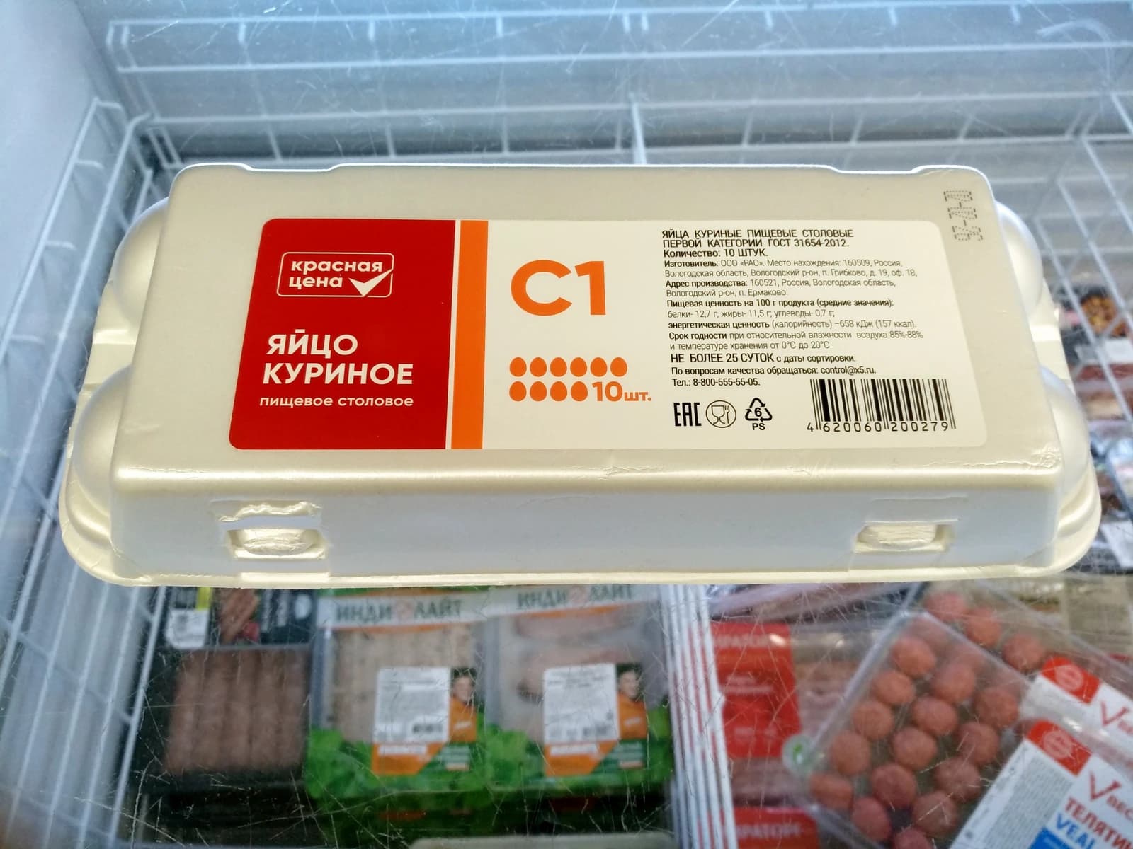 A white carton of Pyatyorochka brand eggs, labeled in Russian, sits in a supermarket refrigerator.