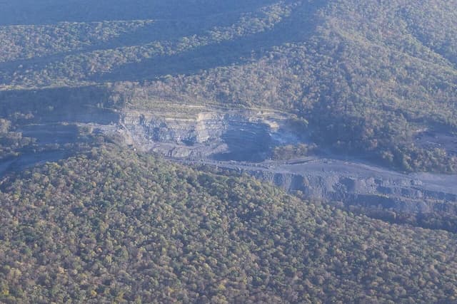 Aerial view of an open-pit coal mine in a forested, hilly region.