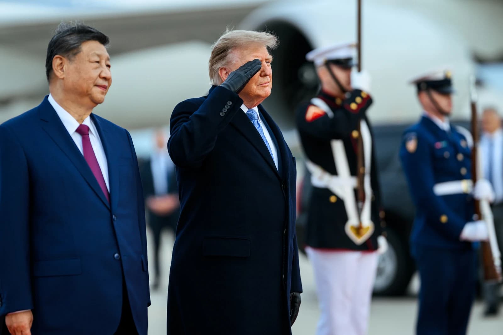 President Donald Trump salutes while President Xi Jinping stands next to him at an airport ceremony.