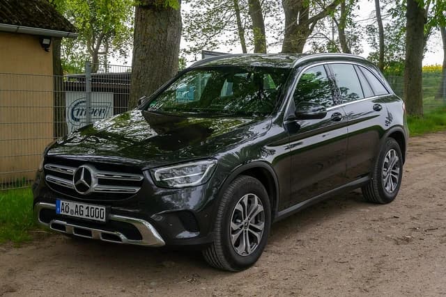 Black Mercedes GLC SUV parked outdoors on a dirt path with trees in the background.