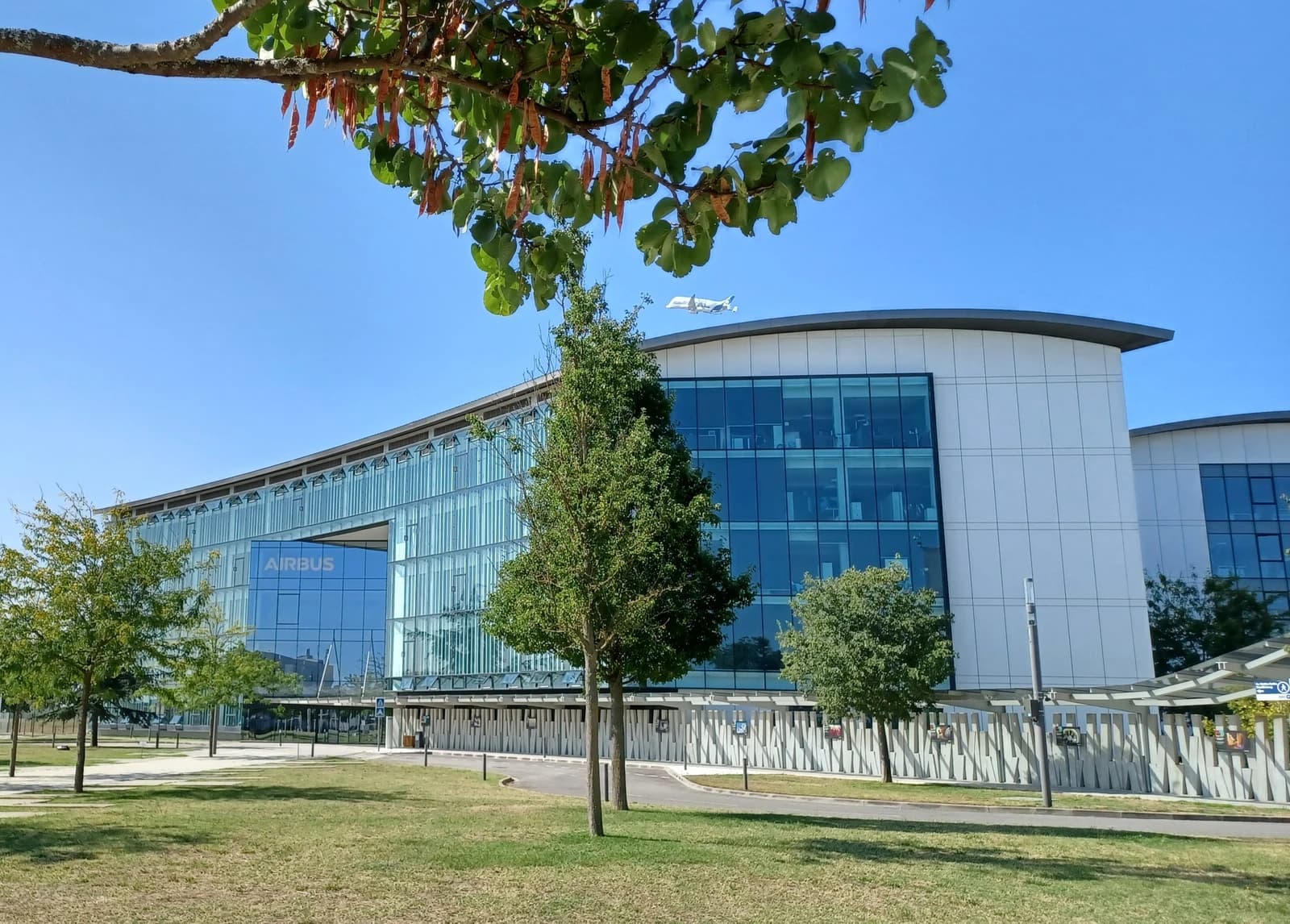 Airbus corporate building in Toulouse, France, with a Beluga airplane flying in the sky.