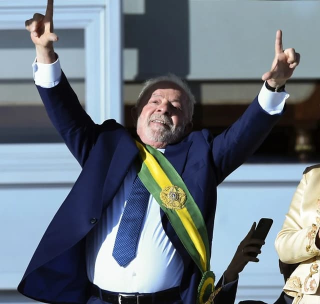 Luiz Inácio Lula da Silva, President of Brazil, stands on a balcony with arms raised.