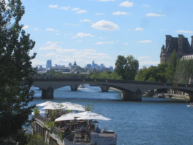 Distant view of modern buildings of La Défense behind a bridge over the Seine River.