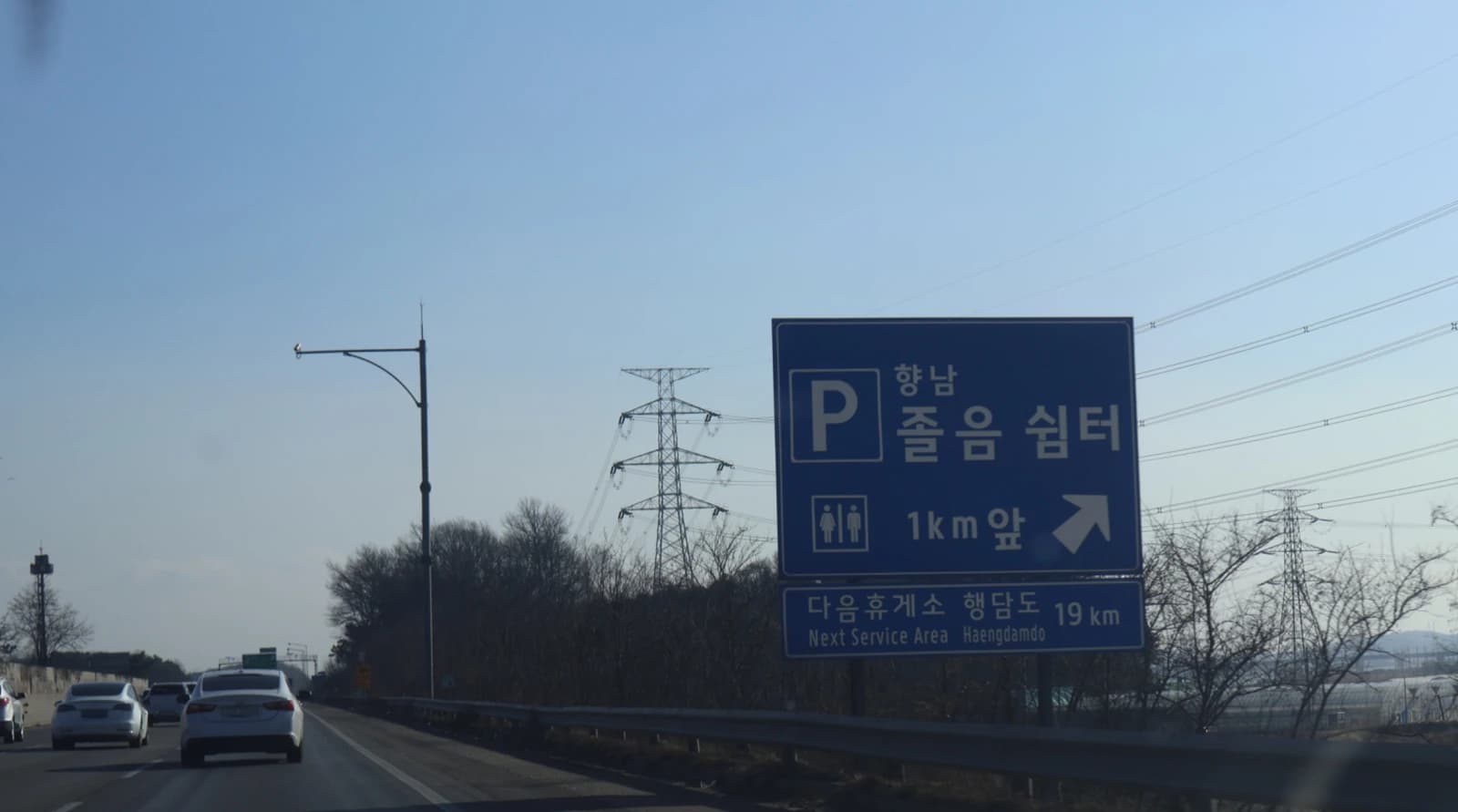 Blue highway sign indicates a rest area 1km ahead on a South Korean expressway.