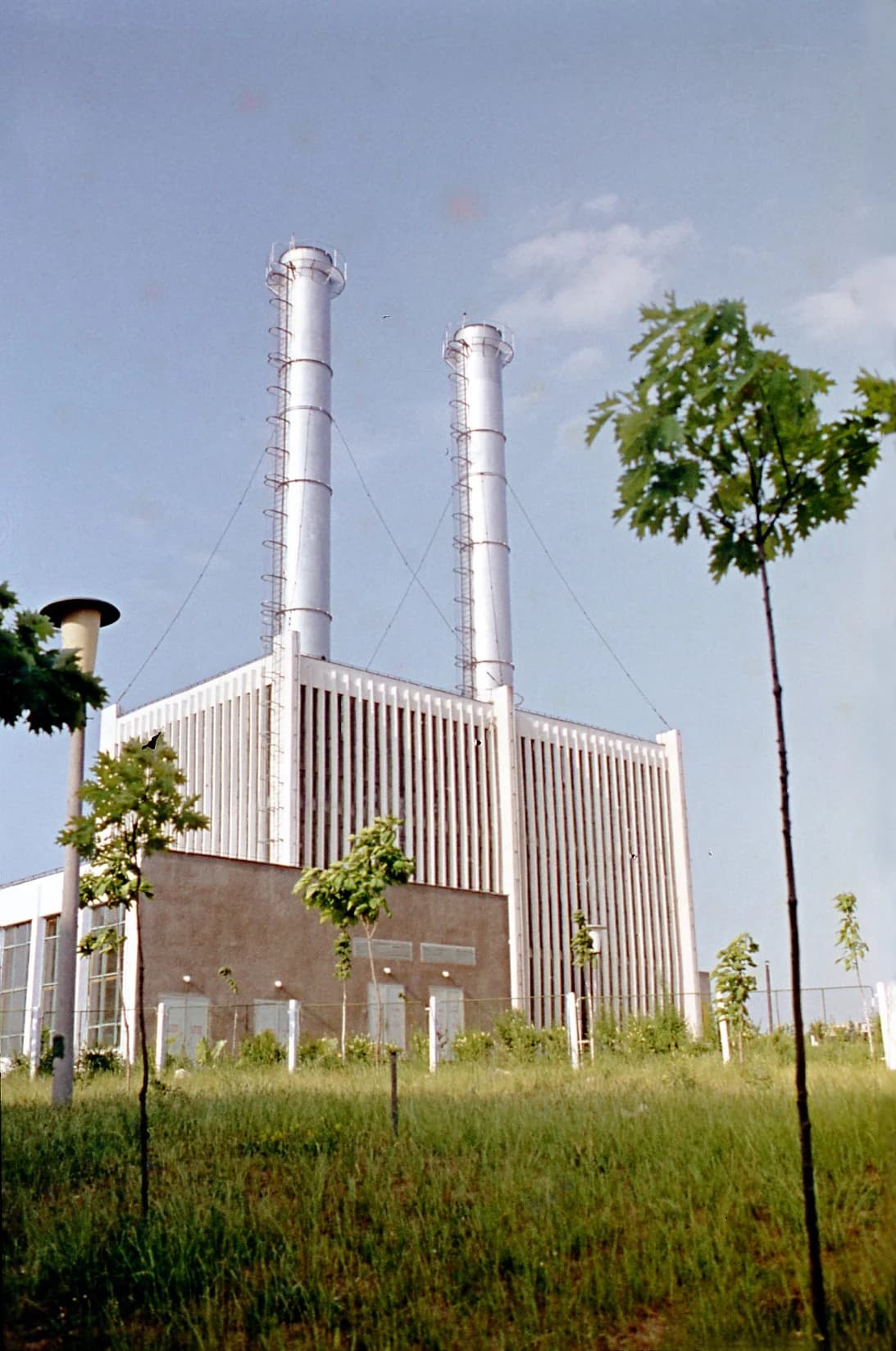Industrial building with two tall chimneys and a grassy foreground under a clear sky.