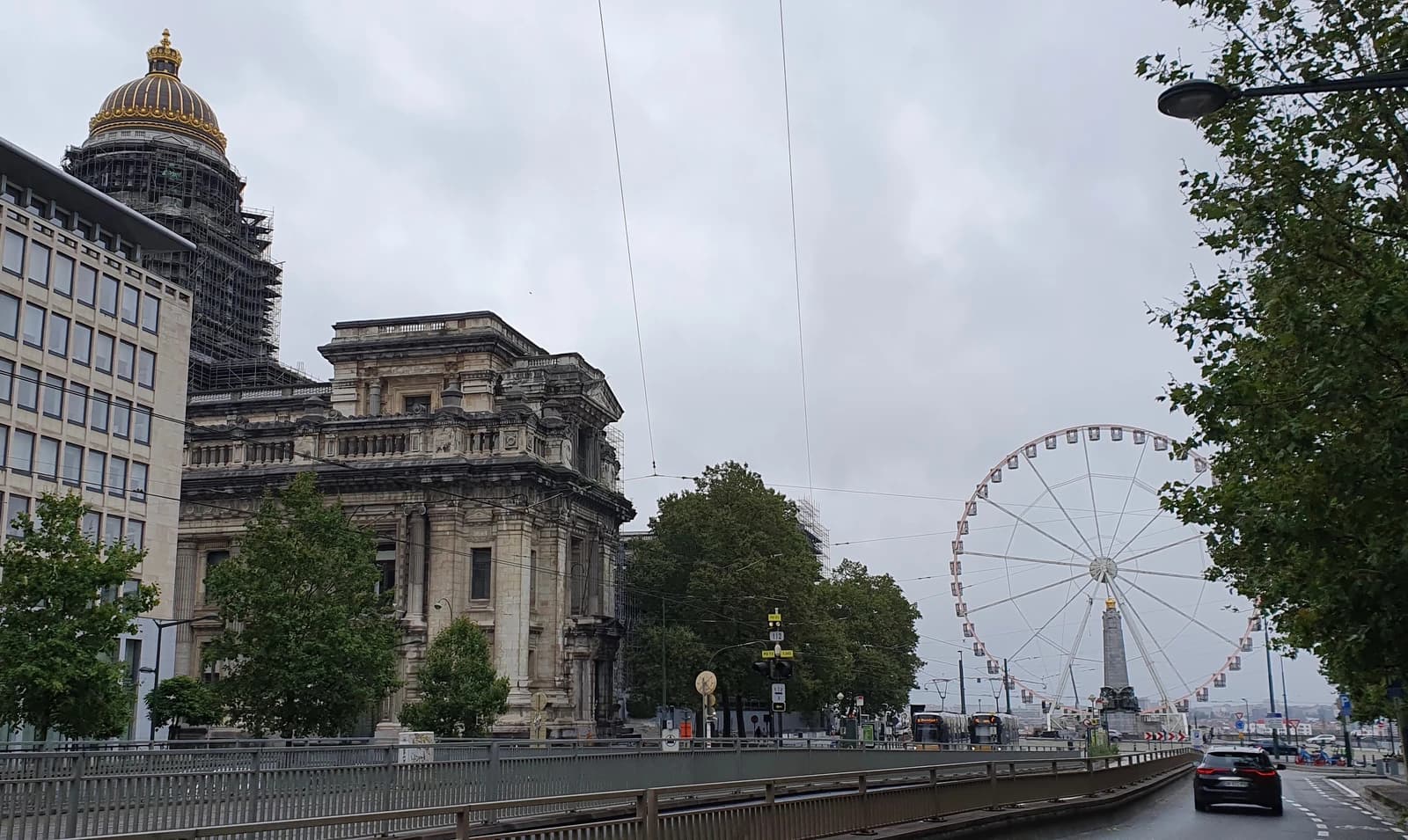 Exterior of the Law Courts of Brussels under scaffolding with a giant Ferris wheel in the distance.