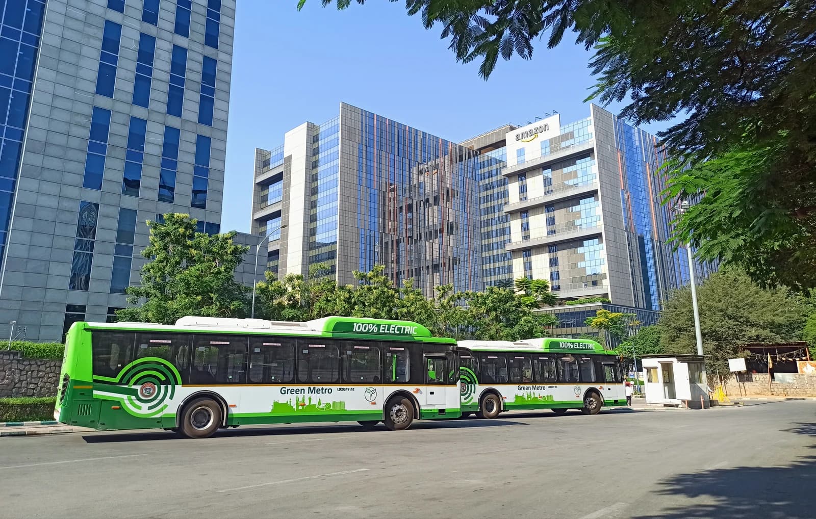 Electric buses parked on a street in front of large office buildings in India.