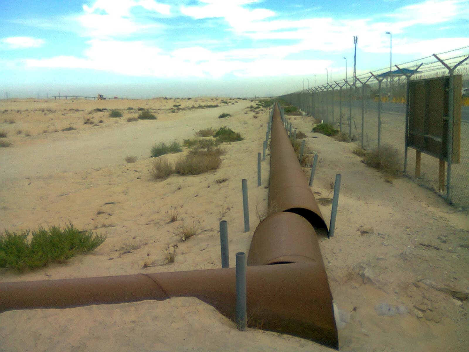 Oil pipelines running alongside a fence in the desert of Jubail, Saudi Arabia.