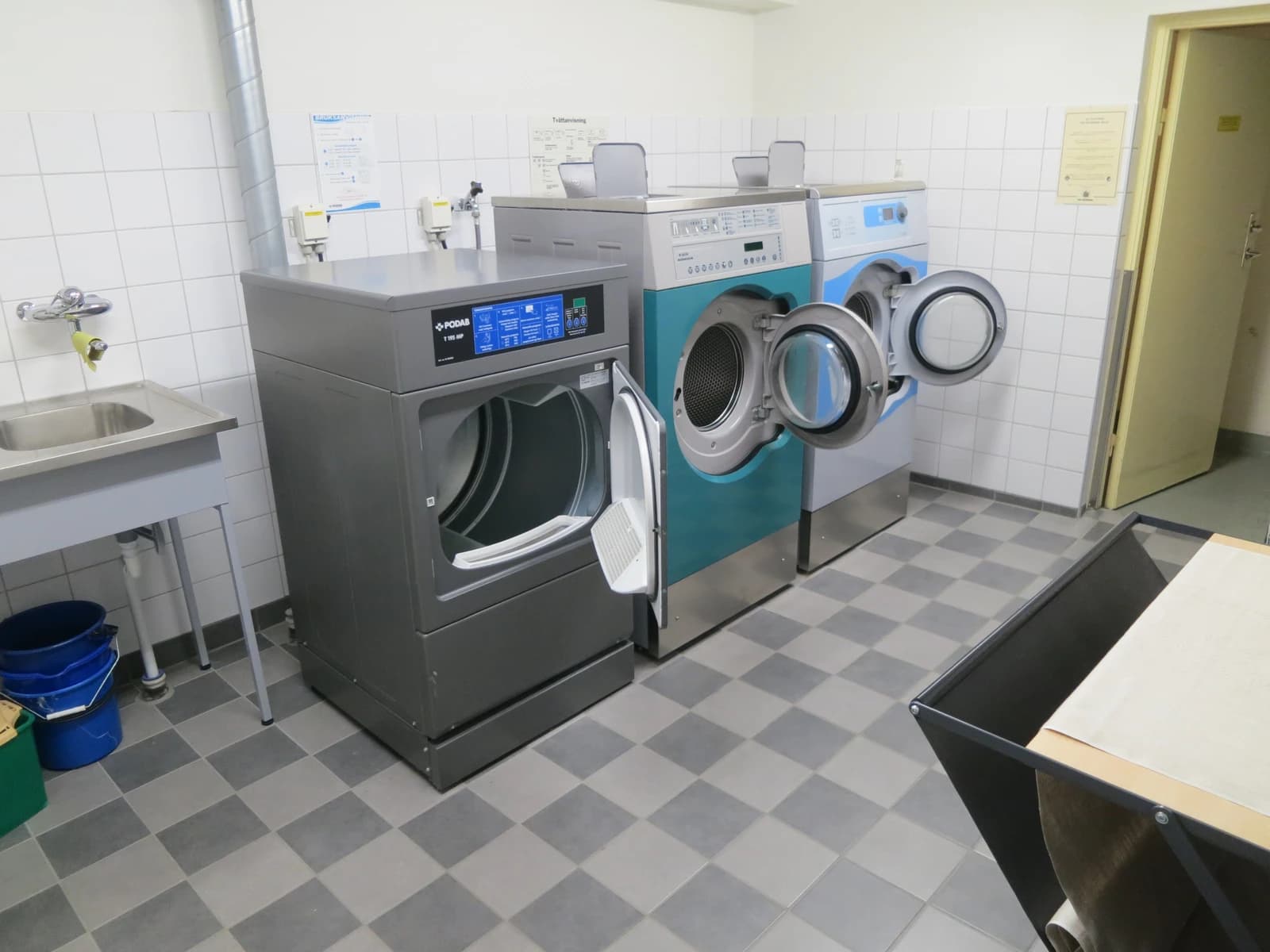 A shared laundry room in a Gothenburg condominium with multiple large washing machines and dryers.