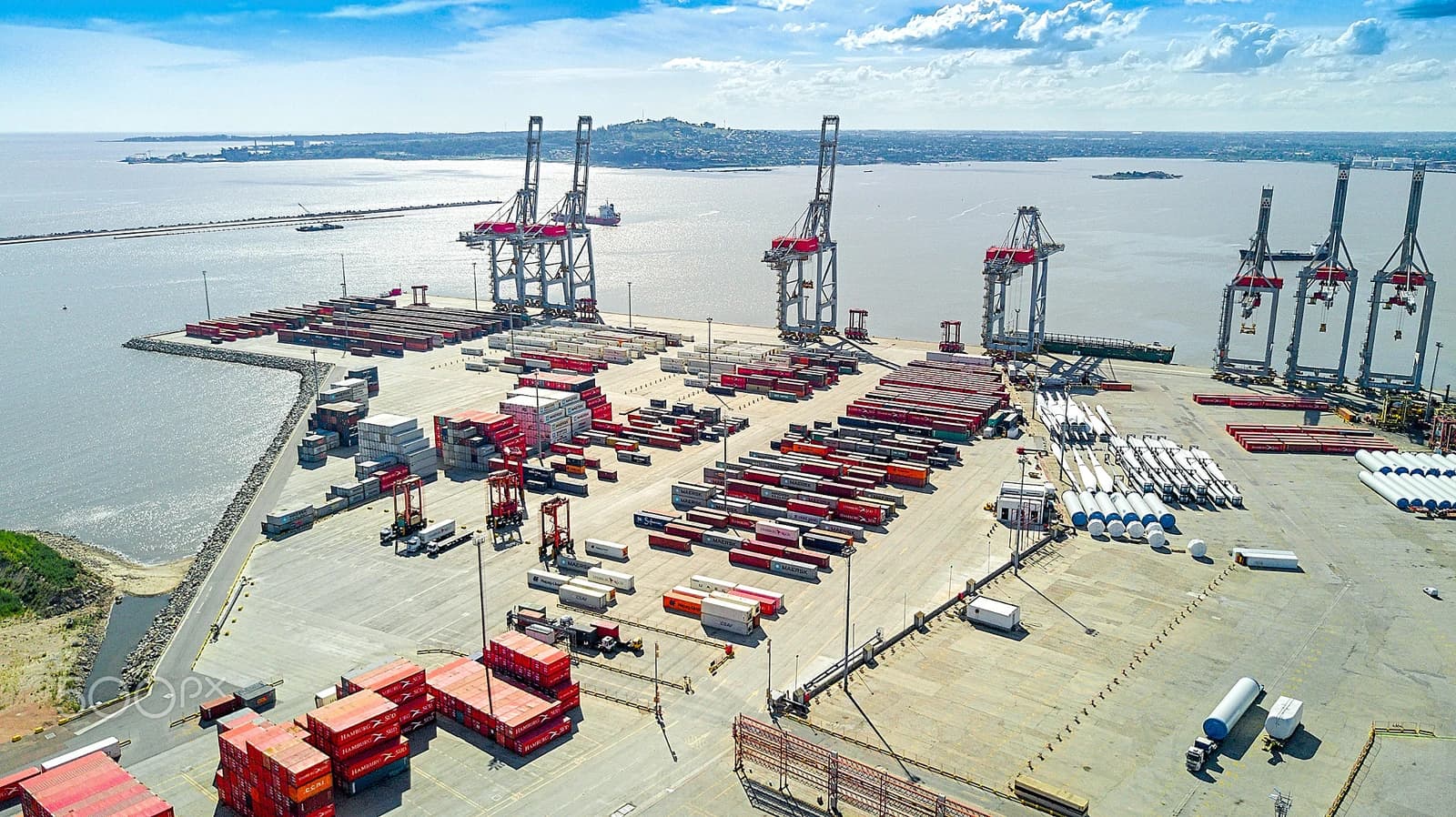 Aerial view of a large cargo terminal with numerous shipping containers and cranes along a coastline.