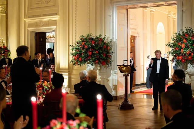 Donald Trump, President of the United States, stands and gestures at a state dinner event.