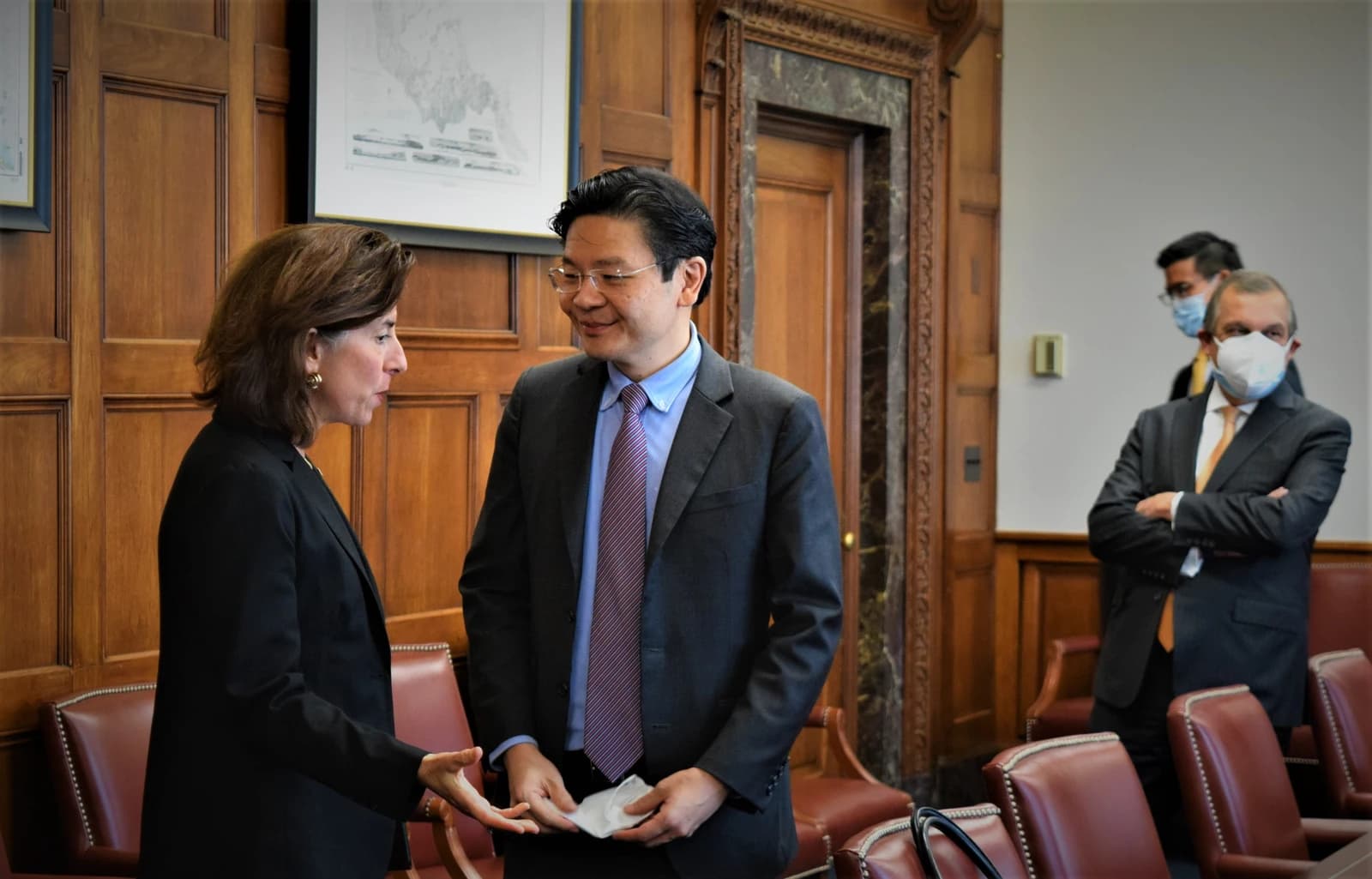 Gina Raimondo speaks with Lawrence Wong in a room with wood-paneled walls.