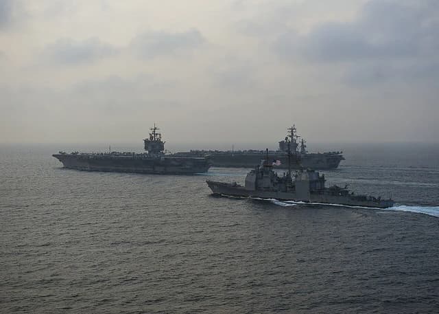 Three U.S. Navy ships, including two aircraft carriers and a cruiser, sailing at sea.