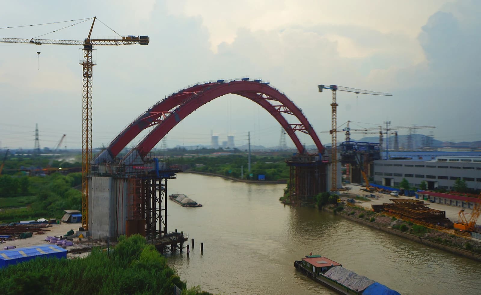 High-speed rail bridge under construction over a river with cranes and industrial buildings.