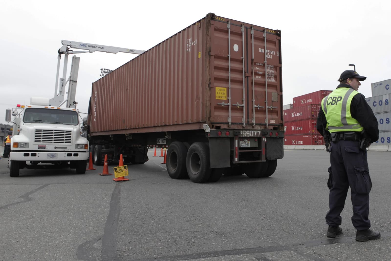 U.S. Customs and Border Protection officer stands near a shipping container being scanned.