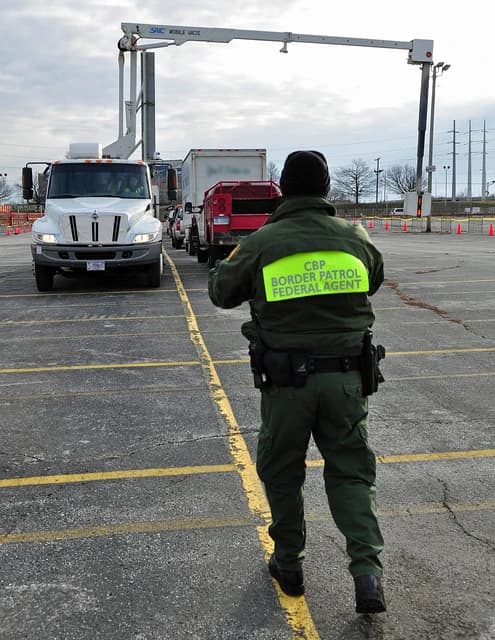 Customs and Border Protection agent supervising cargo trucks at an inspection checkpoint.