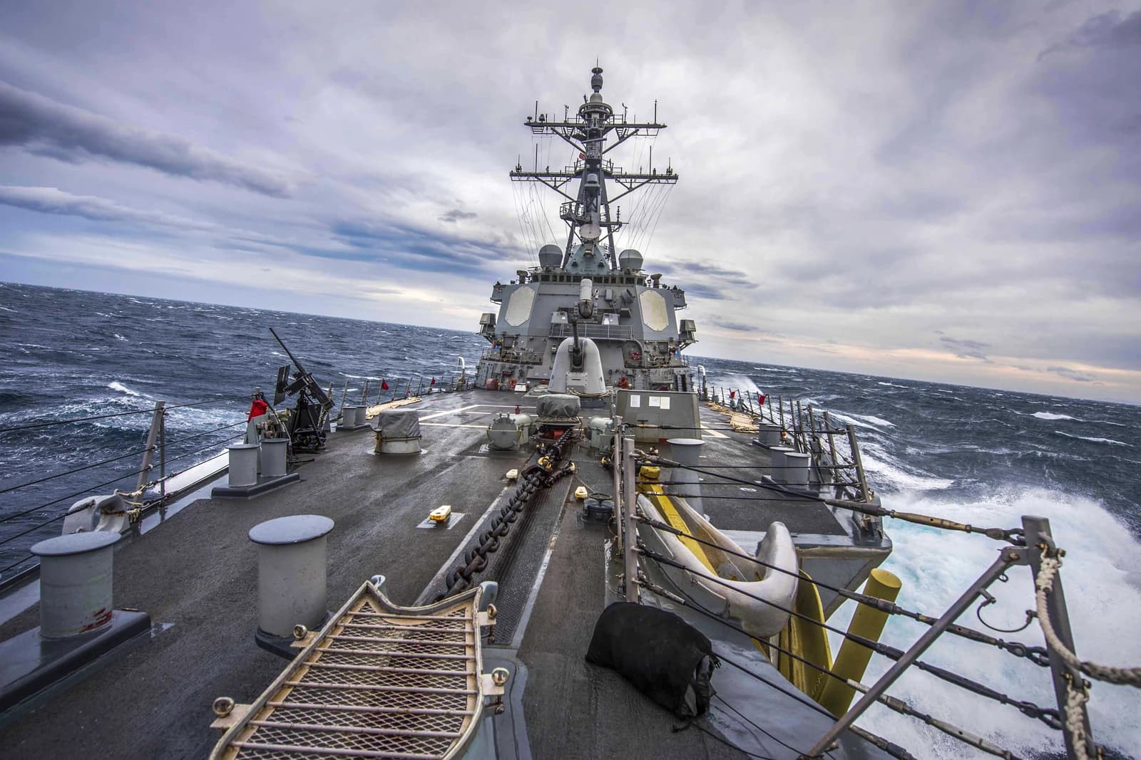 A U.S. Navy destroyer navigating through choppy waters under a cloudy sky.