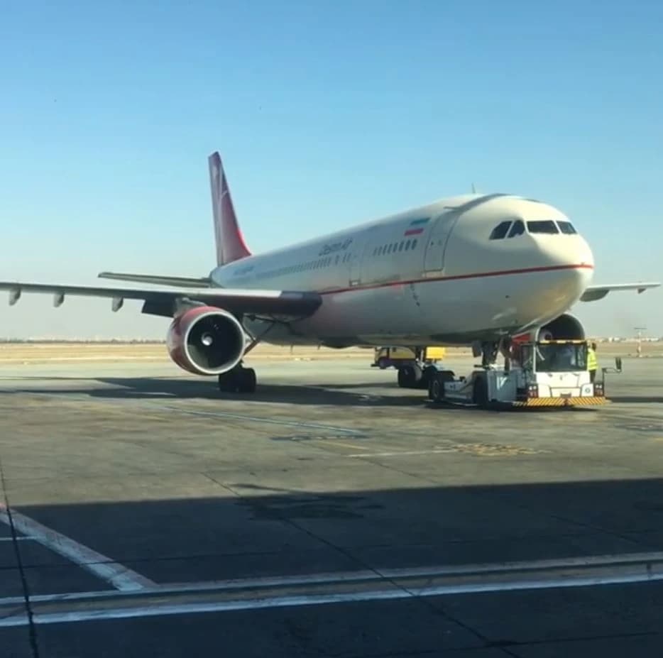 Qeshm Air aircraft on an airport tarmac being pushed back by a tug vehicle.