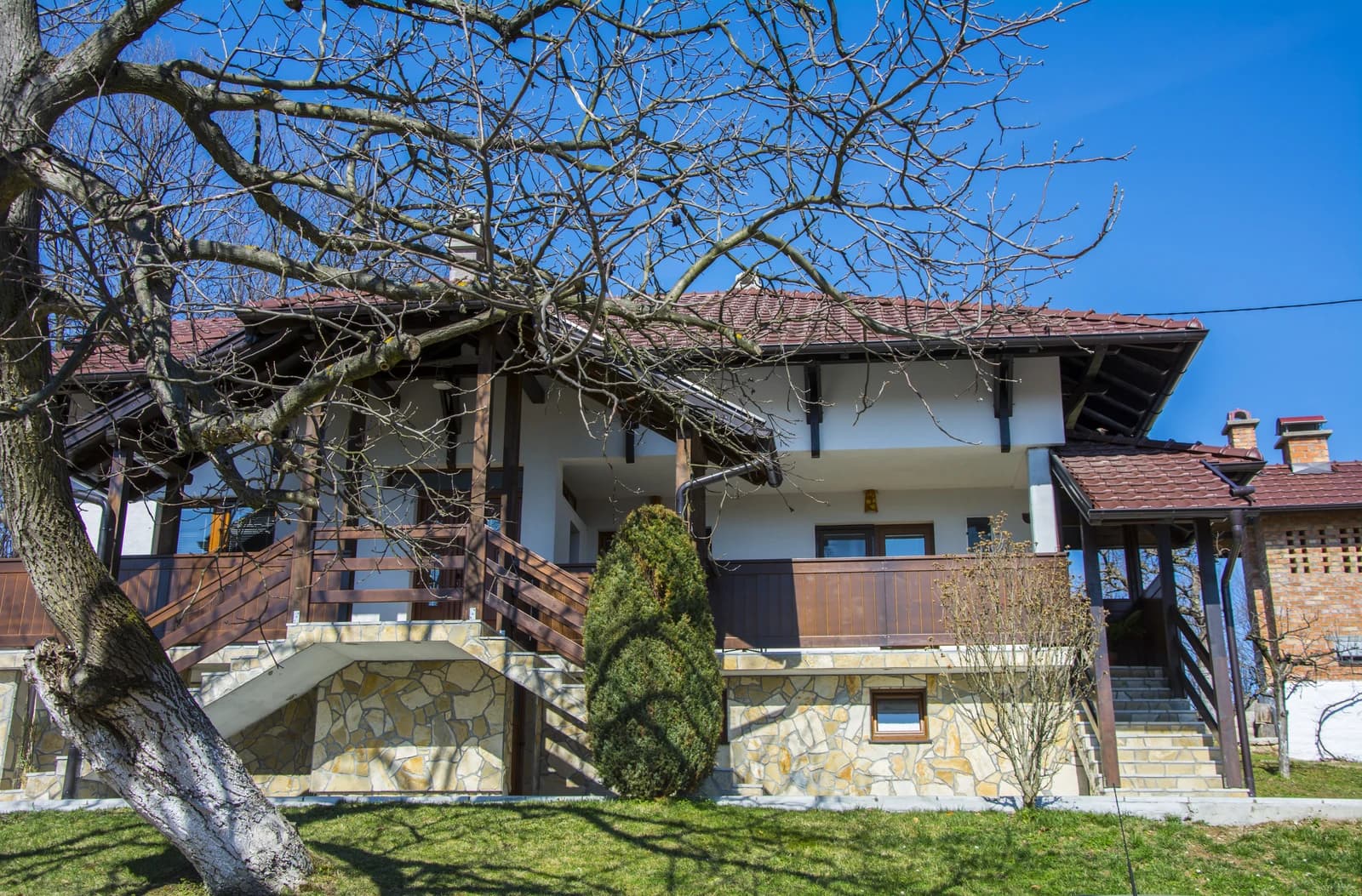 Traditional Serbian rural house with stone facade, brown roof, and wooden balcony.