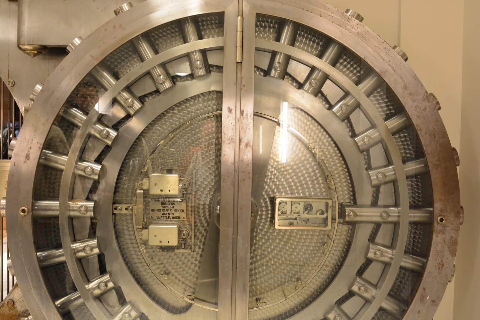 A round, metal bank vault door with a glass panel and visible locking mechanisms.