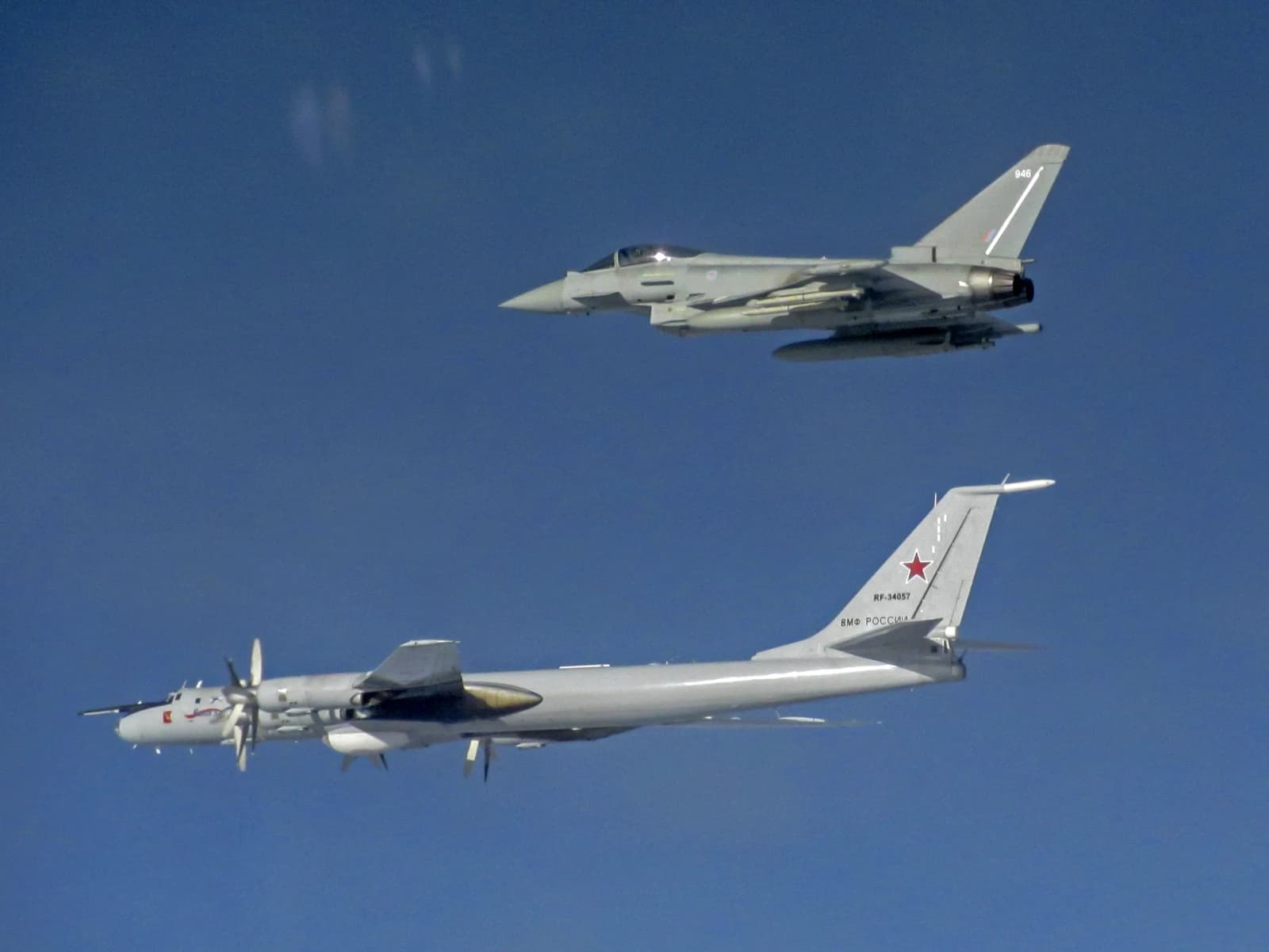 A grey Eurofighter Typhoon jet flies above a grey Russian Tupolev Tu-142 aircraft.
