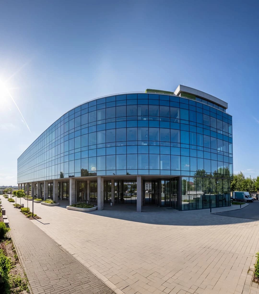 Modern glass business center with curved facade and surrounding paved area.