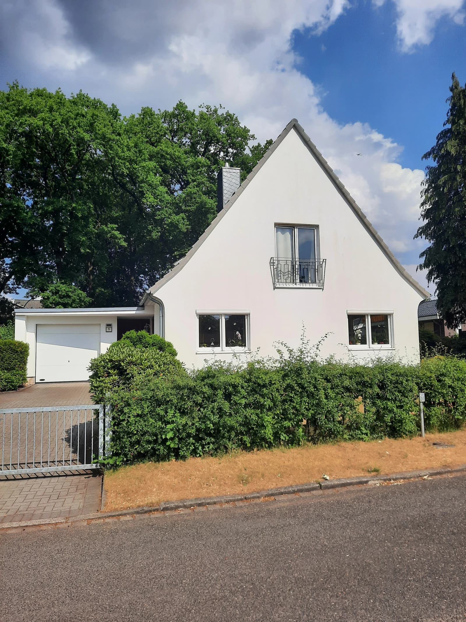 White house with a pitched roof, small balcony, garage, and green bushes.