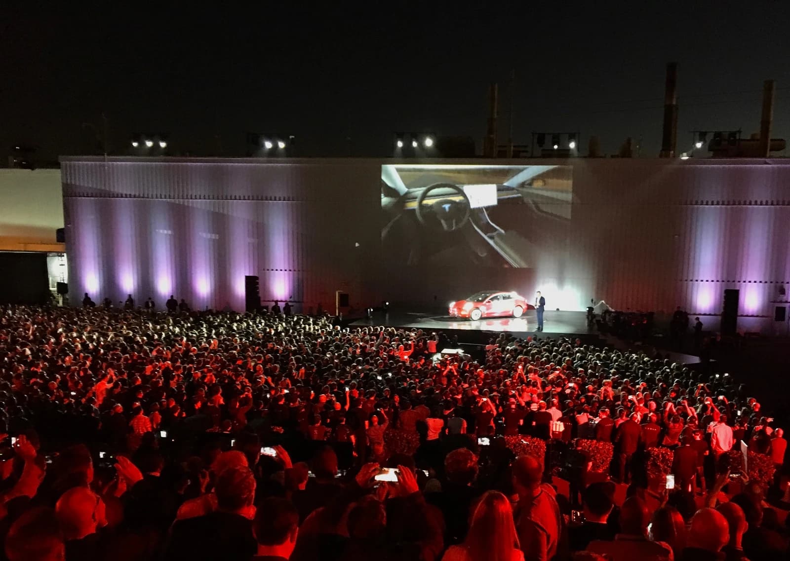 Elon Musk, Tesla CEO, presents the Model 3 electric car on stage to a large crowd.