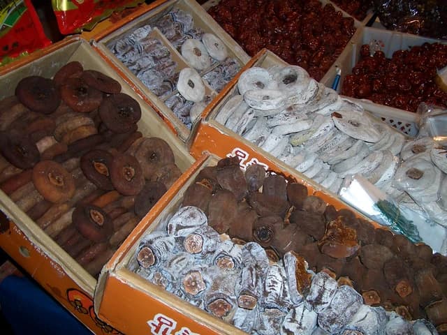 Dried persimmons with white powdery coating and other varieties displayed in wooden and plastic crates.