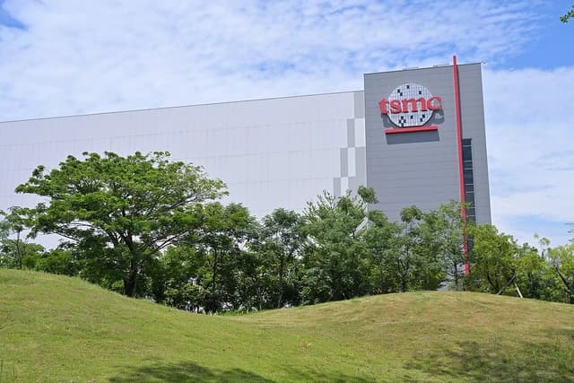 Exterior view of the TSMC AP2 building with green hills and trees in the foreground.