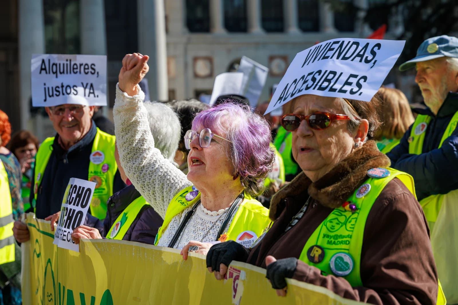Protesters at a demonstration for housing rights hold signs and a banner.