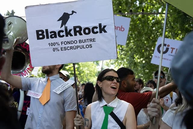 People demonstrating in Madrid, one holding a sign referencing BlackRock and the housing crisis.