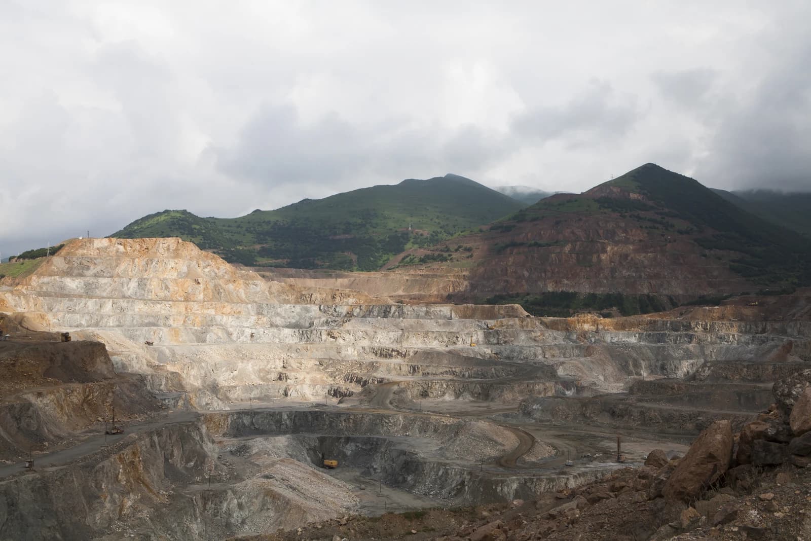 Open-pit copper mine with terraced slopes, mountains, and heavy machinery in Armenia.