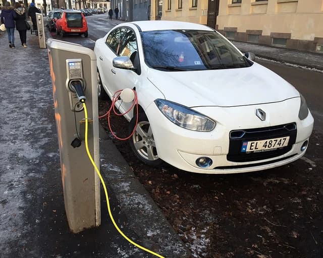 White Renault Fluence Z.E. electric car charging at a public station on a street.