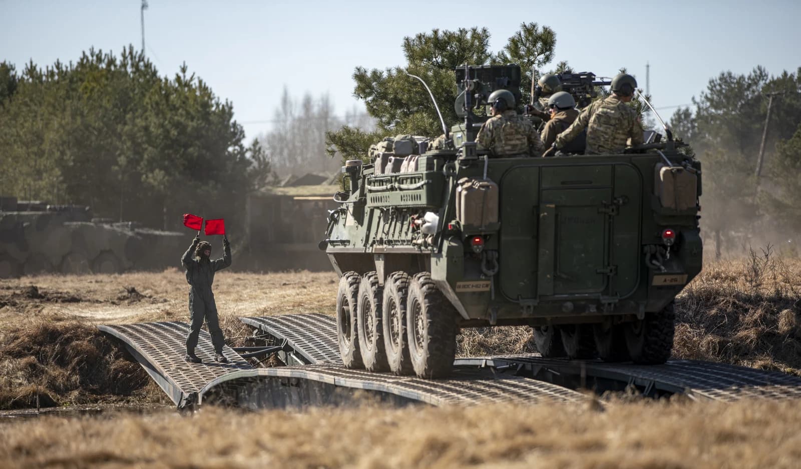 Military personnel on an armored vehicle crossing a temporary bridge during an exercise.